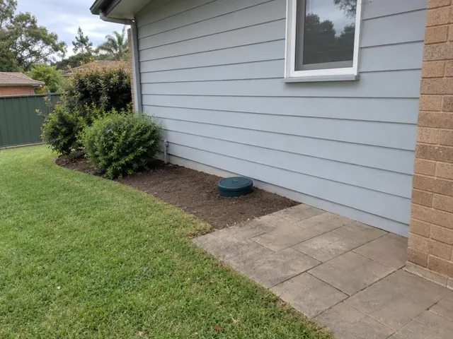 Capped inspection opening beside a house wall with tidy garden bed and paving in Winston Hills